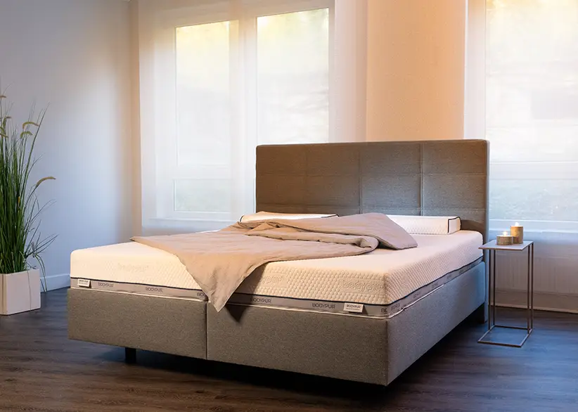 Helles und freundliches Schlafzimmer mit einem Bodypur-Bett, umgeben von sanften Naturtönen und warmem Tageslicht.